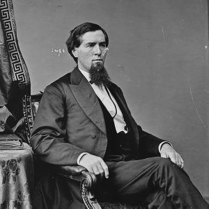 White man with beard in formal attire seated in chair