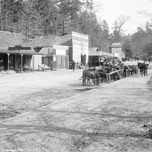 Dirt street with store fronts and horses tied up on the right