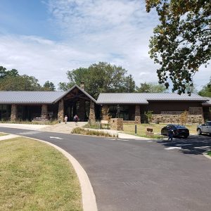 Single-story building with covered entrance supported by rock columns on circular driveway with parking lot