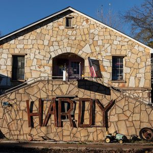 Single-story stone house with "Hardy" sign on double staircase in the foreground