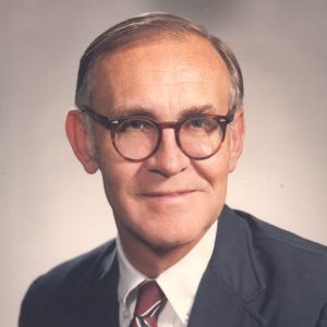 White man with glasses smiling in suit and tie