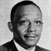 African-American man with mustache smiling in suit and tie