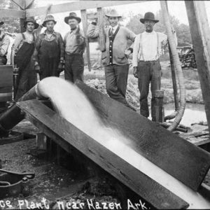 White men standing behind water pump pouring water into a sluice