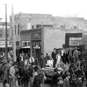 Crowded street with brick buildings and horse drawn wagon