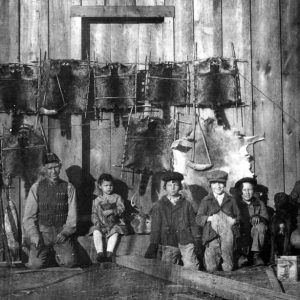 White man and children posing with raccoon hides hanging stretched on wooden walls