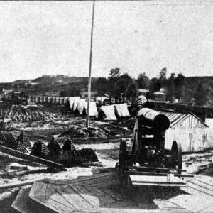 Cannon and cannon balls stacked nearby with buildings and tents in the background