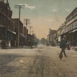 Townspeople walking on street between rows of multistory buildings with power lines