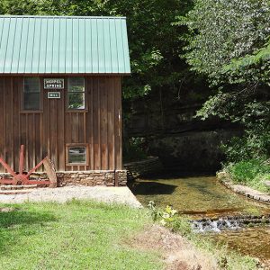 Small mill building with green metal roof and running stream