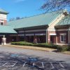 Brick building with green metal roof and clock tower and covered entrance on paved parking lot