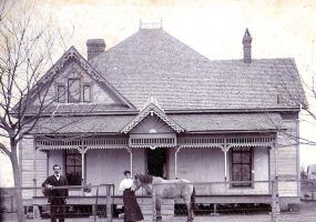 White man woman and horse outside two-story house with fence