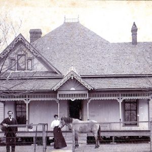 White man woman and horse outside two-story house with fence