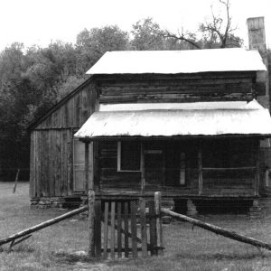 Wooden cabin with covered porch inside wire fence with gate