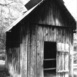 Narrow wooden outbuilding with two slats blocking door opening