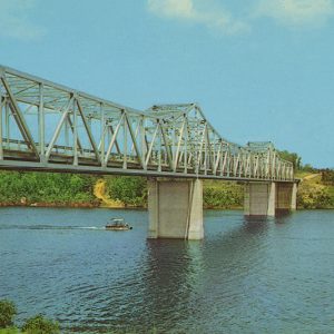 Small boat passing under steel truss bridge on river