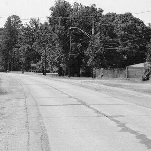 Highway section with fenced-in building on the right and power lines and trees