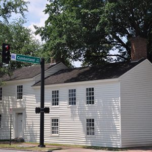 Two-story building with white siding and brick chimney on street corner next to "Cumberland" traffic light