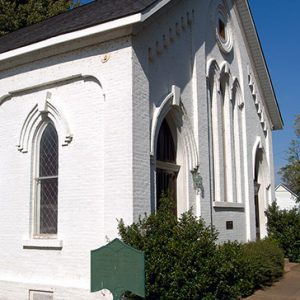 White brick church building with sign and bushes