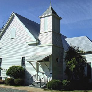 Single-story white building with covered porch and bell tower