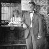 White woman working behind desk with bars and white man in suit standing in the foreground