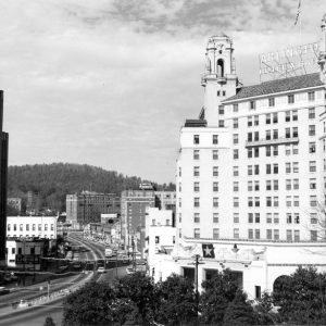 City street with tall buildings and wooded hills in the background