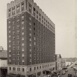 Tall building with many windows on street corner with cars and people