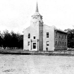 Multistory building with steeple tower and multistory building behind it on dirt roads