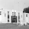 Two-story brick building with monument, flagpoles, and trees