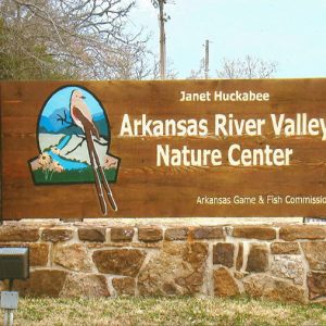 Bird on a branch over a river on wooden sign with white text and stone base