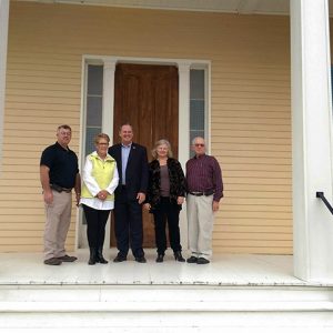 Three white men and two white women standing on covered porch at front door of multistory plantation house