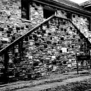 Close-up of multistory building with stone walls and double staircase with "Hughes" sign in front of it