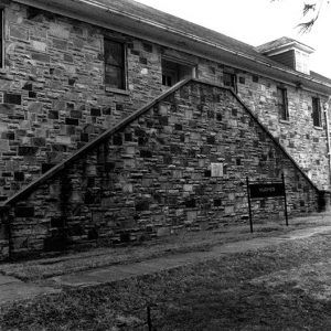 Close-up of multistory stone building with double staircase and "Hughes" sign in front of it