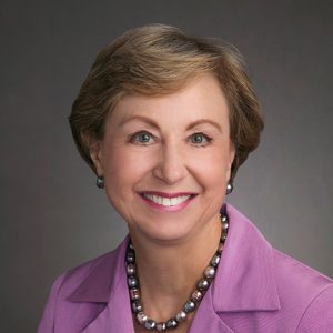 White woman smiling in pink suit and necklace