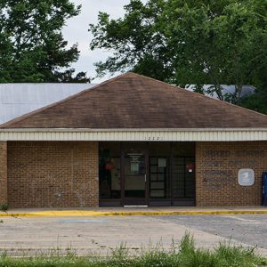 Single-story brick building on parking lot with blue mail box