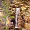 tourists walking under natural waterfall with tree in pool