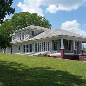 white house with covered porch and brick stairs with another house behind it and blue skies