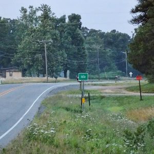 "Ida" road sign on two-lane highway with mobile homes in the background