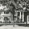 Multistory house with covered porch supported by four columns and trees on street