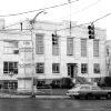 Multistory stone panel art deco building with monument in front and station wagon hanging stop lights and street signs