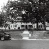 Multistory building with two wings behind trees with sidewalk and steps leading to parking lot