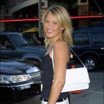 White woman smiling in pants tank top purse posing by stanchion red rope street traffic