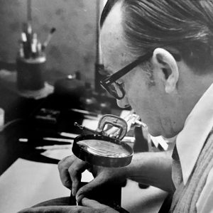 Older white man with glasses using a magnifying glass to work on a woodcut