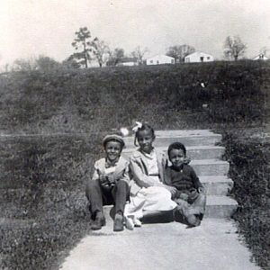 Three African-American children sitting on steps with houses in the far background