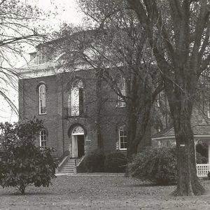 Multistory brick building with steps on grass with tall trees