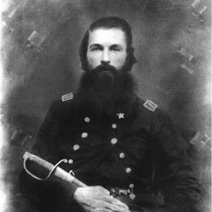 White man with long beard sitting in military uniform holding a sword across his lap