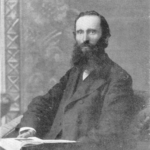 White man with long beard sitting in chair with open book