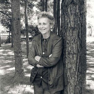 Older white woman with arms crossed leaning against a tree