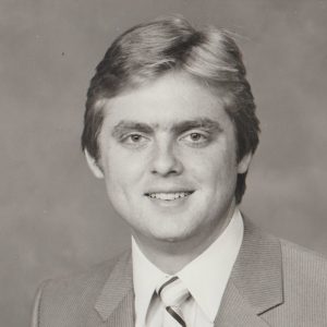 White man with short hair smiling in suit and tie