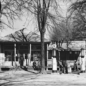 Single-story gas station with pumps and three trees on dirt road