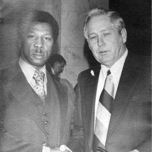 African-American man with mustache in suit standing next to older white man in suit and tie