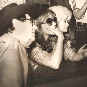 White man with cowboy hat and glasses sitting at table with white woman with sunglasses and white woman with curly hair